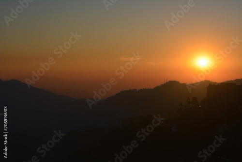 A vibrant, hazy sunset over silhouetted, rolling mountain ridges, creating a warm, golden atmosphere for creative projects, wellness content, or as a background, the beauty of the natural environment