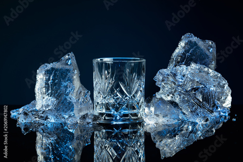 Cuadro en lienzo Crystal glass of vodka and ice shards against a black reflective background