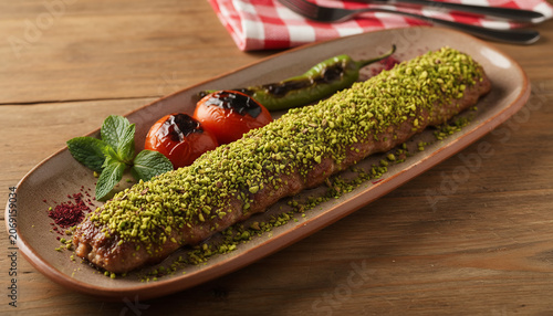 Traditional Turkish Adana kebab coated with crushed pistachios, served on a rustic platter, blending authentic Anatolian cuisine with gourmet presentation.