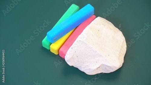 natural pieces of chalk, mineral stones and multicolored school chalk on green chalkboard background, concept, top view, rotation