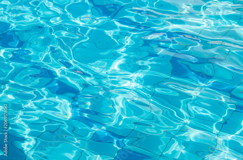 Side view of a blue-tiled outdoor swimming pool with crystal-clear water, shimmering and sparkling in the sun. Abstract water texture background.