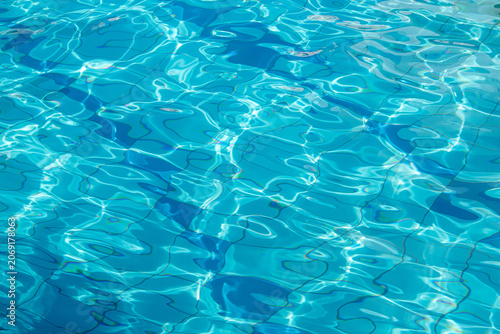 Side view of a blue-tiled outdoor swimming pool with crystal-clear water, shimmering and sparkling in the sun. Abstract water texture background.