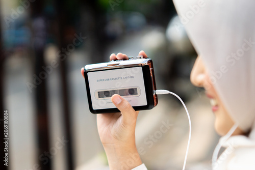 Young Asian Muslim woman enjoying and listening to music with portable retro stereo cassette