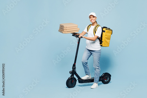Delivery woman wear white cap T-shirt uniform yellow thermal food bag backpack work as dealer courier ride e-scooter hold pizza in cardboard flatbox isolated on plain blue background. Service concept.
