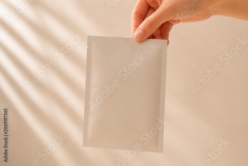 Blank Cosmetic Sachet Mockup Held By Hand On Neutral Background