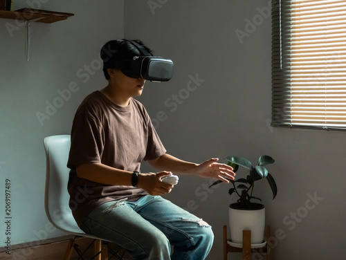 Asian person sits at home wearing VR glasses using advanced technology to browse the web play immersive games and enjoy interactive digital entertainment with fun and communication.