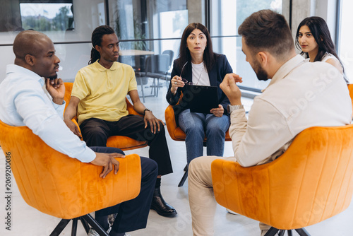 фотографія Diverse adults engaged in group therapy session for mental health support, discu