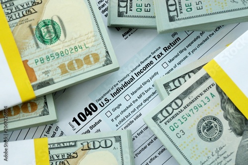Photos 1040 Individual Income tax return form and hundred dollars money bills packs on