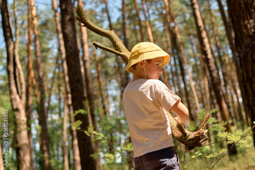 Obraz na płótnie A child stands in a forest, holding a branch