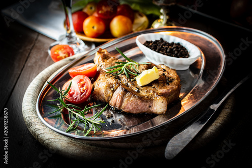 Fotografie Romantic candlelit dinner featuring a perfectly grilled pork neck steak on a vintage metal platter, served with red wine, fresh rosemary, and ripe tomatoes in a warm, rustic atmosphere