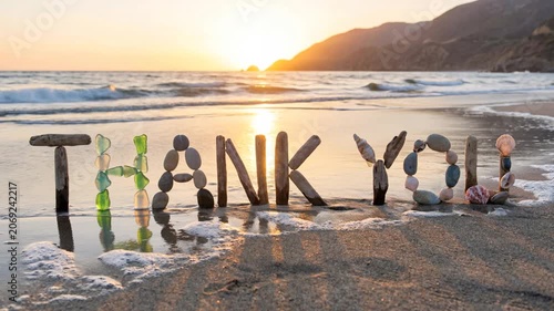 Thank you word formed with driftwood, sea glass, pebbles, and shells on a beach at sunset, showing gratitude message Concept Video
