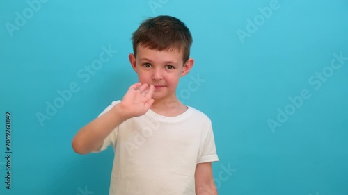 Little child boy waving hand to greet someone. Cheerful kid gesturing say hello or goodbye. Friendly male character on blue background for social communication and childhood concept.