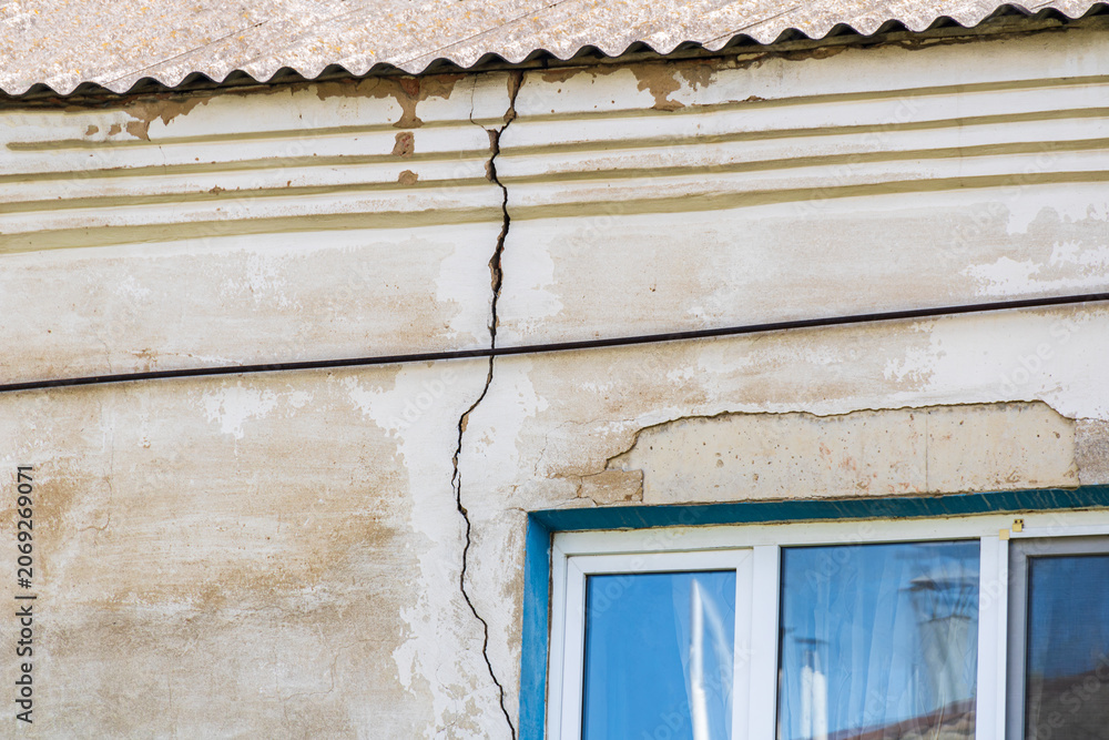 Fototapeta premium Severe vertical crack in stucco wall of old house above window, concept of building foundation failure, structural damage inspection, insurance claim and real estate defect assessment background