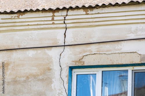 Fotografía Severe vertical crack in stucco wall of old house above window, concept of build