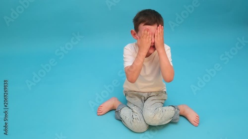 Sad boy sitting on floor covering his face with hand. Upset child expressing frustration or feeling lonely. Emotional outburst, grief and mental health concept for child psychology.
