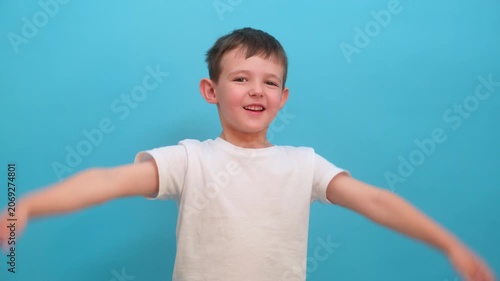 Happy boy gesturing with hands up. Child showing joy and excitement against blue background. Childhood expression, energy and lifestyle concept. Portrait of kid greeting or celebrating.