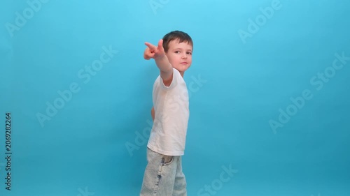 Child pointing finger while looking at camera on blue background. Small boy in white t-shirt showing direction. Young schoolboy expressing choice or sign. Advertising concept for kid model.
