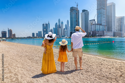 A beautiful tourist family walks at a city beach with view of the Dubai Marina skyline, UAE