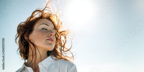 Sensual young woman with long, vibrant, wavy curly red hair and natural freckles, closed eyes peacefully, standing, relaxing, enjoying under the bright warm glow of the summer sun outdoors,  copyspace