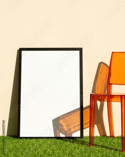 Blank vertical frame mockup leaning on green turf grass with orange acrylic chair
