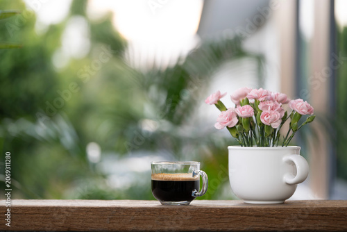 Coffee and pink flowers in a white vase on wooden table