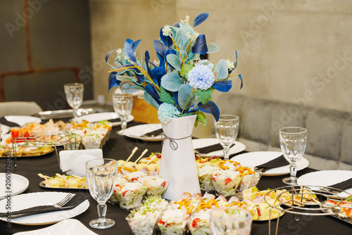 Banquet table setting with catering snacks and beautiful blue flower bouquet