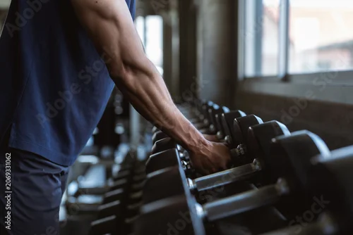 Panel kuchenny z motywem Close up of strong sportsman arm holding heavy dumbbell iron piece. Active male exercising power strength routine at indoor sport club fitness