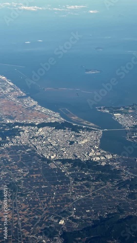 Aerial coastal tracking sequence showing airplane approach over peninsula cityscape harbor and port infrastructure during bright daylight revealing urban expansion