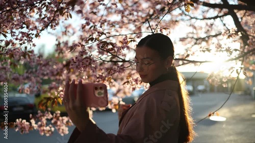 young woman taking selfies among blooming cherry blossom trees enjoying spring season and capturing memorable moments in a colorful park setting