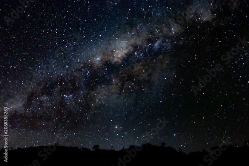 Quadro su tela Breathtaking view of the Milky Way galaxy glowing brightly with countless stars in a deep dark night sky over a black desert landscape
