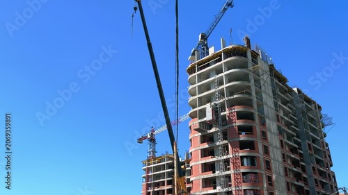 High-rise residential building under construction with elevator rising and tower crane against clear blue summer sky