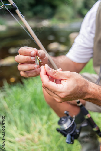 vertical Hispanic fisherman preparing fishing lure by river
