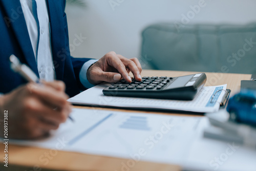 Fotografie Businessman using a calculator and writing on financial documents at desk for ca