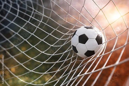 Soccer ball in the goal net close up of a football hitting the net after a goal, with a blurred stadium background and warm sunlight