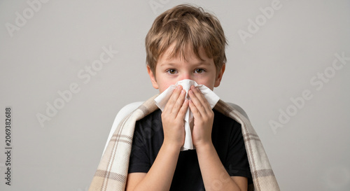 Sick little boy with catarrh symptoms blowing his nose into a tissue