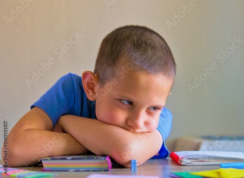 Close-Up of a Sullen and Bored Young Boy Resting on His Crossed Arms, Ignoring His Homework