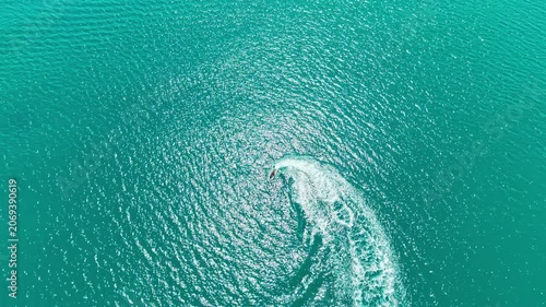 A speedboat travels swiftly on bright blue ocean water during the day. The sun reflects off the surface, creating sparkling patterns.