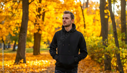 Young man in black hoodie standing in autumn park with golden leaves falling, enjoying the season