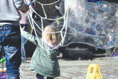 A cheerful little girl chasing big soap bubbles outside in vintage film color grading.