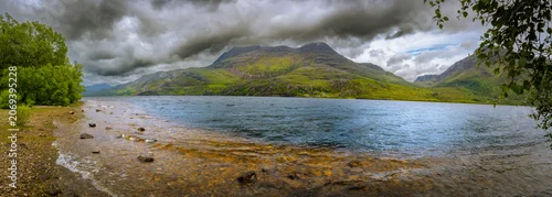 Panel kuchenny z motywem Glistening waters of Loch Maree reflect the towering green mountains while dark clouds hover above creating a captivating atmosphere