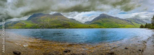 Panel kuchenny z motywem Glistening waters of Loch Maree reflect the towering green mountains while dark clouds hover above creating a captivating atmosphere