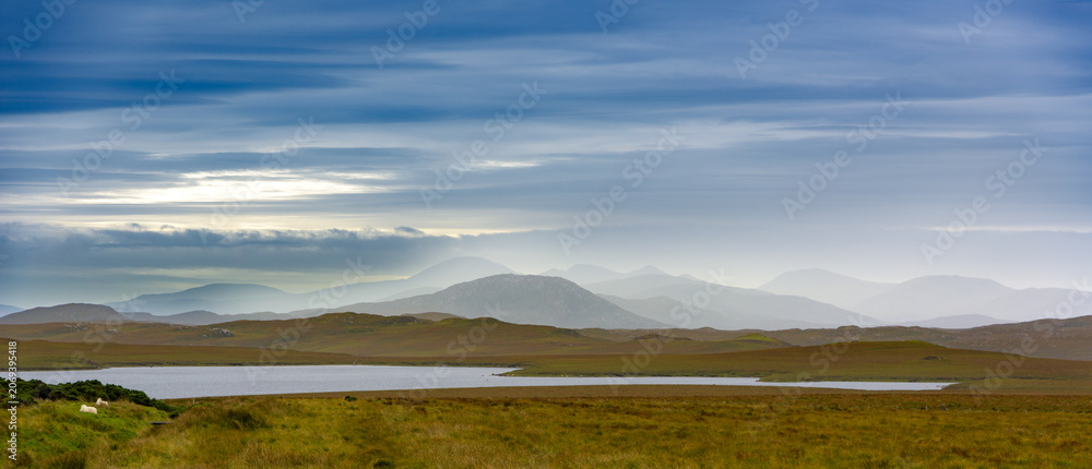 Fototapeta premium A calm evening view features rolling hills and a peaceful lake under an expansive sky with soft muted colors