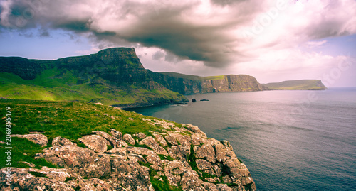 Schilderij op canvas A stunning view from Neist Point showcases towering cliffs against a backdrop of dark clouds with calm waters reflecting the fading light
