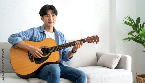 Young man playing acoustic guitar sitting on a sofa, enjoying a hobby, practicing music at home