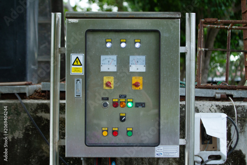 Electrical control panel cabinet switch button indicator warning mounted outdoors on industrial equipment, stainless steel enclosure with meters and lights, safety maintenance concept