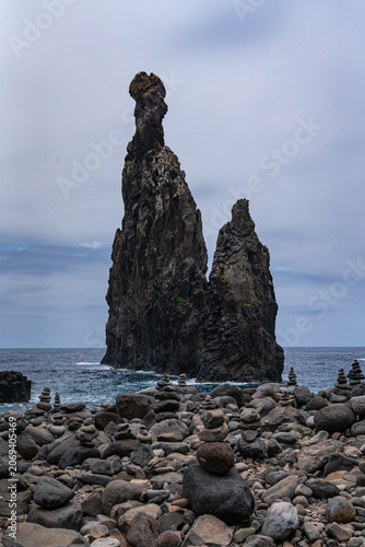 Volcanic rock formations in the ocean with stone troll houses  on Ribeira da Janela beach, Porto Moniz, Madeira Island, Portugal on a cloudy summer day.