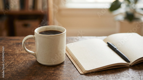 Coffee mug beside open notebook with pen