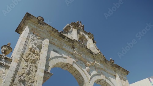 Aerial drone shot looking up at the Zapopan Arch, capturing its decorative columns and eagle sculpture at the top against a vivid blue sky in Guadalajara, Jalisco