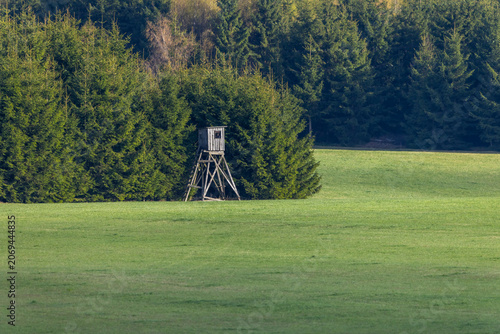 Wooden hunting stand in a green field bordering forest in Czechia