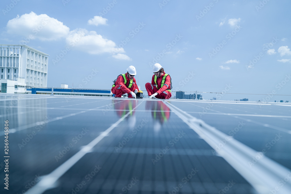 Fototapeta premium On-site view as a field engineer in red coveralls and a hard hat leans over the array to inspect a module atop a commercial building, capturing clean energy, sustainable power.